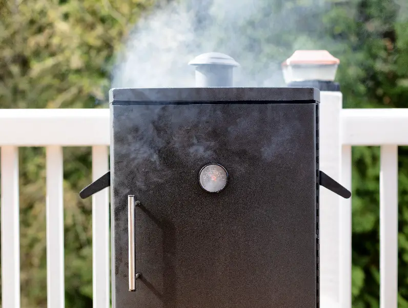 Close up of a cooking smoker with woods in background