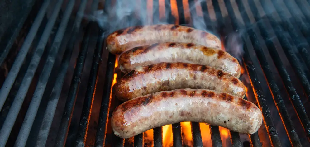 The brats are cooked on a grill with flame and smoke