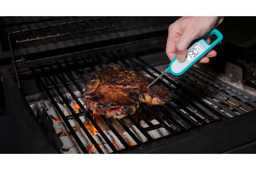 Cook measuring temperature of freshly grilled steak on hot barbecue grill