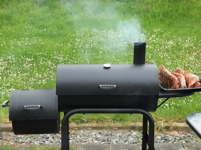 A smoker grill placed outdoors by Pioneer Smoke Houses that has smoke coming out of it. 