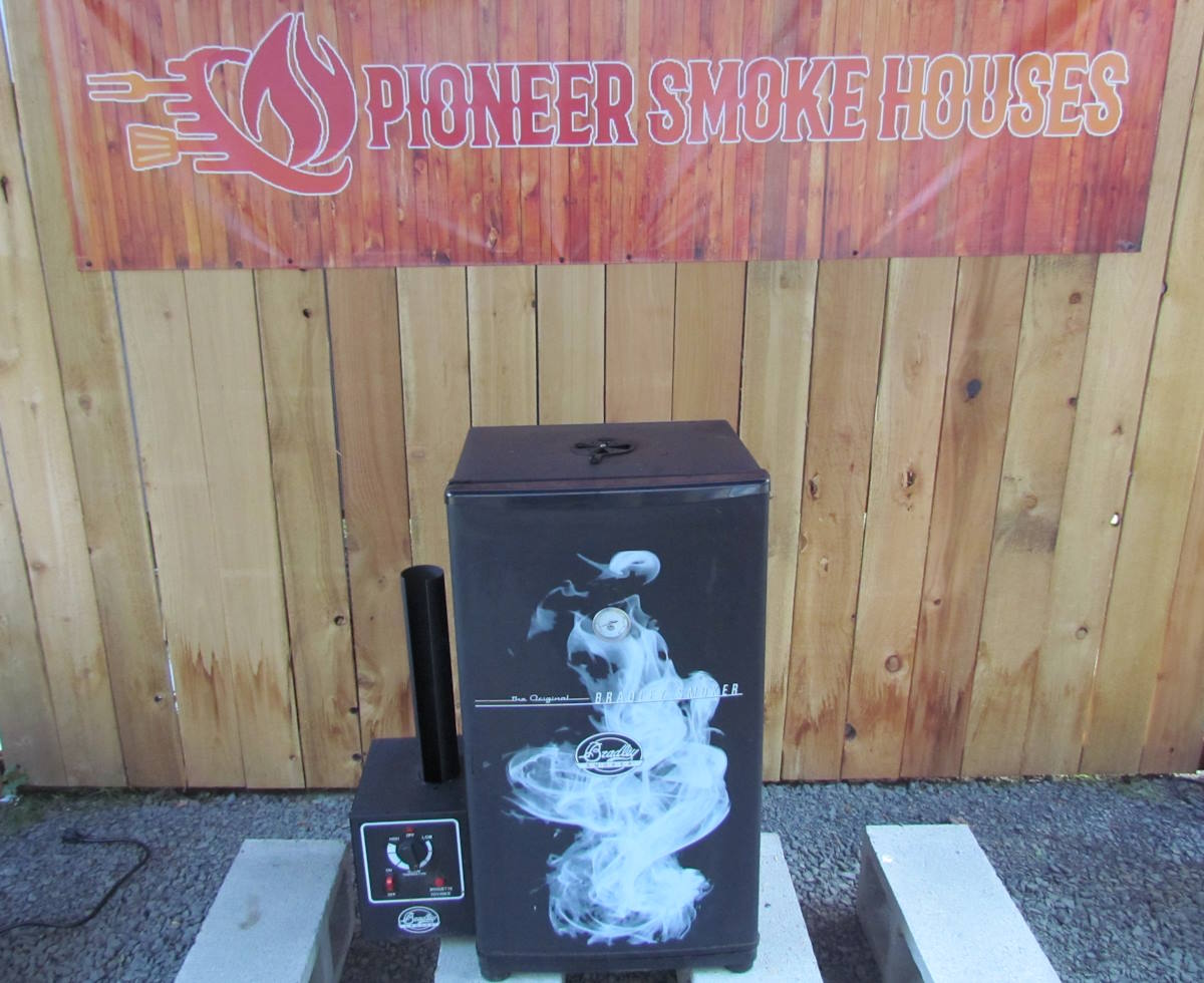 The Bradley Electric Smoker set placed against a white background is being reviewed by Pioneer Smoke Houses.