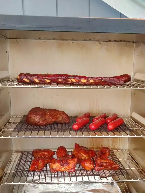Different cuts of meat loaded onto the grill racks in an electric smoker
