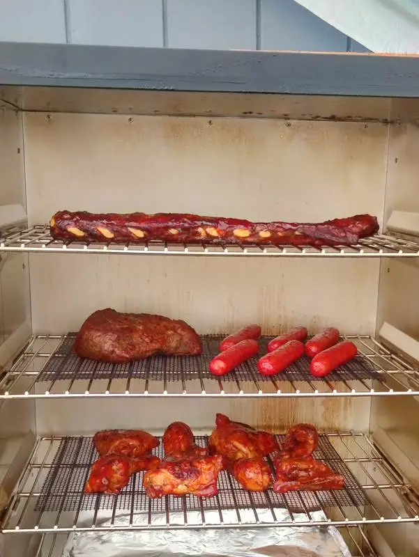 Different cuts of meat loaded onto the grill racks in an electric smoker